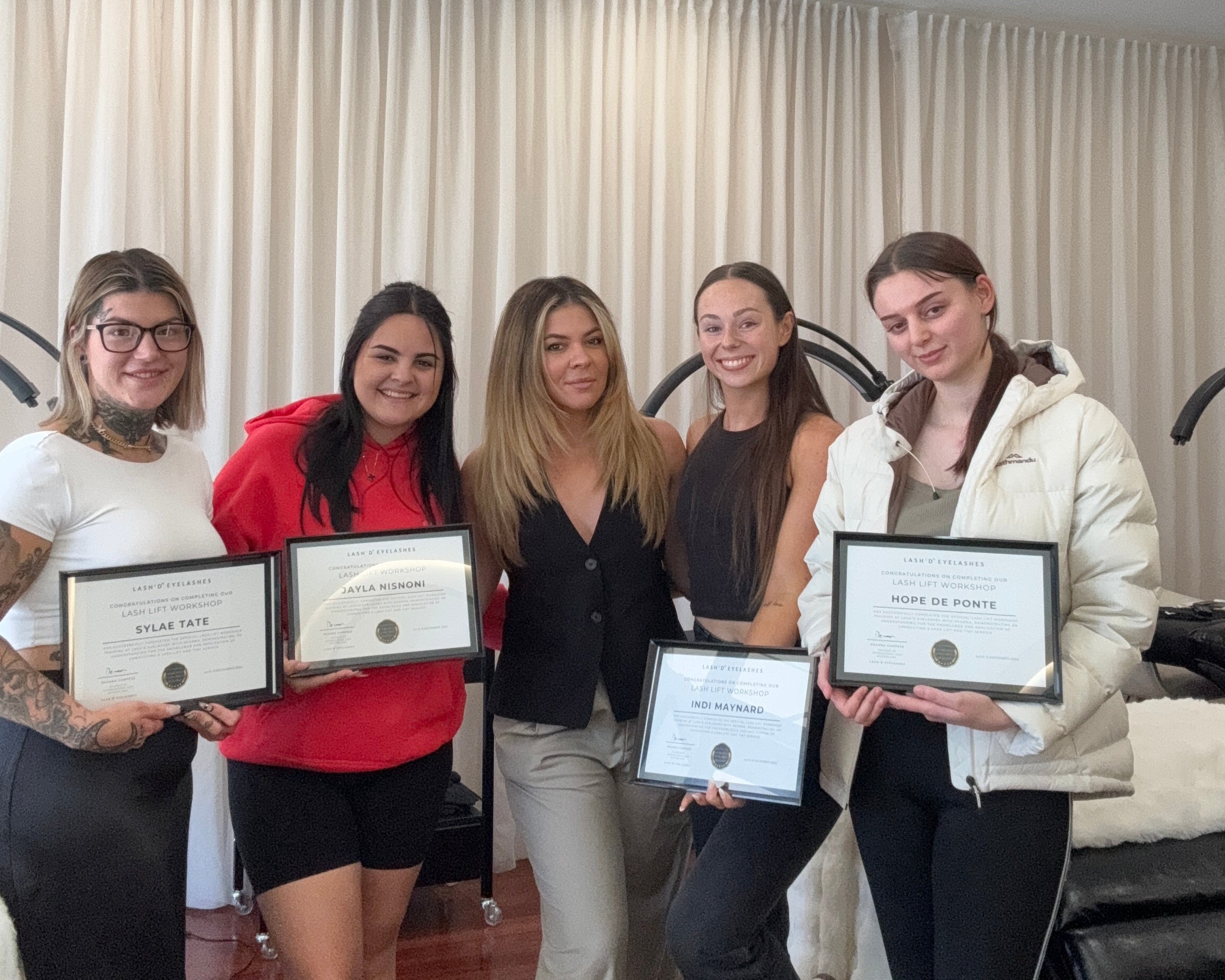 Group of people holding lash lift certificates in an indoor setting